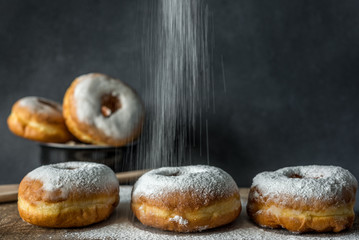 Lush sweet homemade donuts sprinkled with powdered sugar on a wooden background
