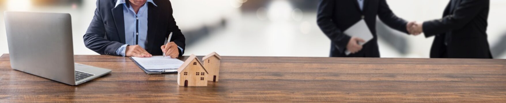 real estate, property and home owner signing contract by bank agency concept, small wooden house model on office table with signing on rental agreement paper to rent above mentioned residence