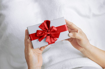 Elderly women hands holding gift box with red ribbon and Sleep on the bed with a white blanket