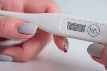 Close up: woman hands holding white digital medical thermometer with high temperature - selective...