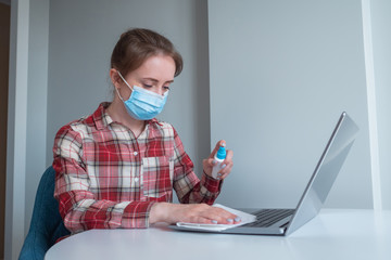 Woman in medical face mask spraying antiseptic, cleaning laptop keyboard with disinfectant wet wipe. Disinfection, protection, prevention, housework, COVID 19, coronavirus, safety, sanitation concept