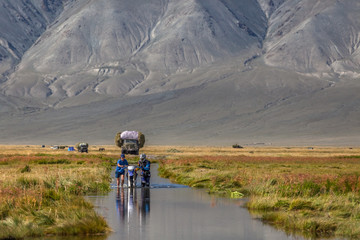 Two men are pushing a motorcycle along a road flooded with water. Altai, Mongolia.