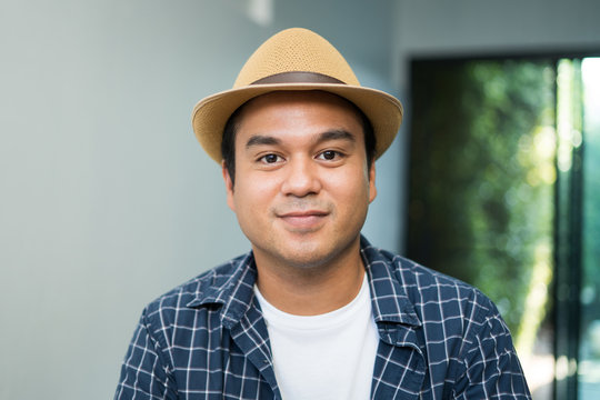 A young asian man, around 30 years old, good-looking, wearing a hat, wearing a blue shirt Sit and work at home