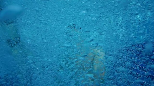 Slow motion video of man diving underwater in aqua park pool releases air during dive. Air bubbles floating from seabed to surface of water