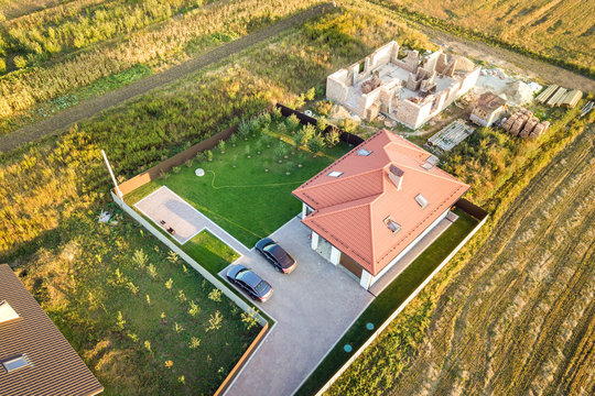 Top down aerial view of two private houses, one under construction with concrete foundament and brick walls and another finished with red tiled roof.