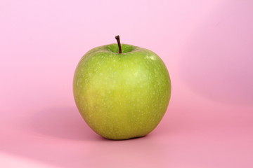 Green yellow apple on a pink background. Juicy ripe beautiful fruit.