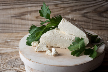 home-made Adyghe cheese cut into pieces on a wooden stand on a wooden background, decorated with fresh parsley leaves