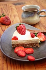 Strawberry cheesecake on light blue plate on wooden table. Rustic mug with milk and strawberry on the side. Closeup, vertical.