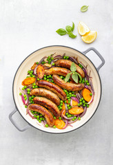 Sausages sauteed with green peas red onions and carrots, top down view
