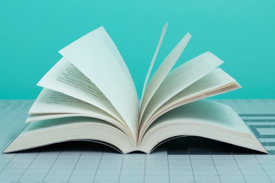 Closeup Of An Open Book On The Table Under The Lights Against A Blue Blurry Background