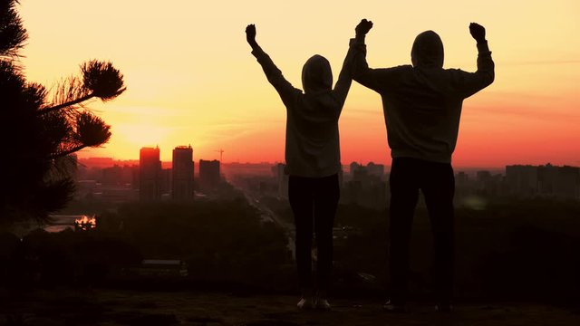 silhouette couple or friend in casual hoodies celebrate win looking on the cityscape at sunrise urban town view in the morning sky with rising sun
