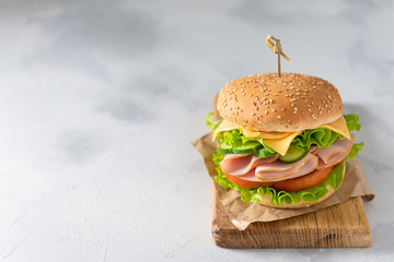 Sesame seeded sandwich with ham, lettuce, cheese and tomato on wooden board on gray background. Copy space
