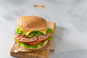 Delicious sandwich with fresh vegetables, cheese and ham on wooden board on gray background. Side view, copy space. Menu, recipe