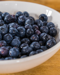 Fresh blueberries in a white bowl on a wooden table. 5x4.