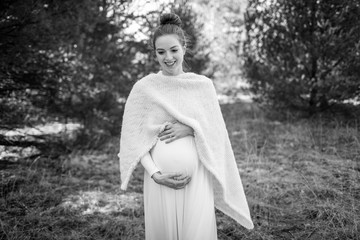Pregnant woman in a white dress and poncho outdoors.  Black and white image.