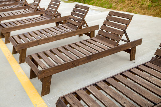 Row of empty wooden beach chairs near water outdoors.