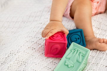 Closeup of baby hand grabbing rubber block in a selective focus, infant sitting on a white blanket...