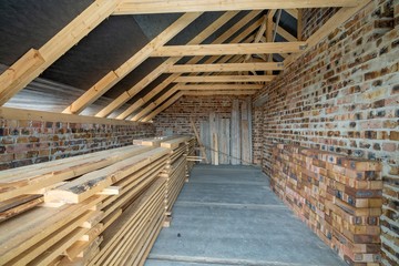 Interior of unfinished brick house with concrete floor, bare walls ready for plastering and wooden roofing frame attic under construction.