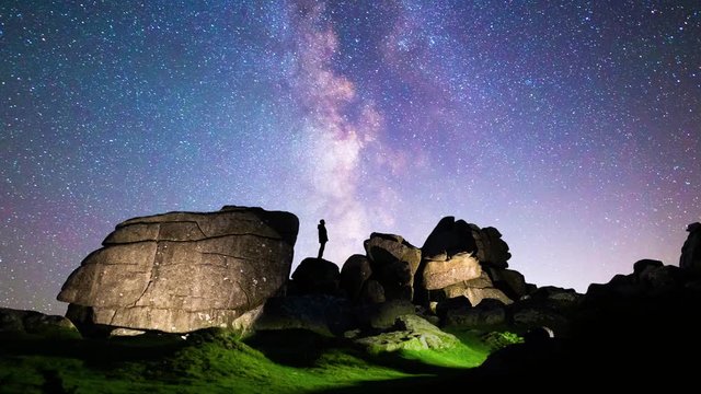Silhouette of a figure stargazing beneath the Milky Way in Dartmoor National Park, with lighting painting of rocks and landscape