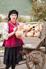 Beautiful girl in national dress. Holding an ancient pot in his hands. Antique clothing of the late 19th century. Beautiful dress and skirt on a woman. The concept of rural life, national traditions