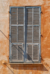 Alter, hellblauer hölzerner Fensterladen in orangfarbener Hausfassade