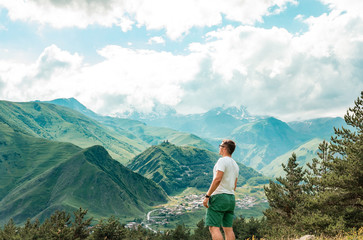Naklejka premium young man standing on the background of the Caucasian mountains. Male man enjoy with mountains and cloudy sky. Travel, Lifestyle adventure vacations concept