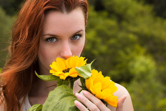 Mujer joven peliroja muy bella oliendo girasoles en el campo y mirando seductoramente