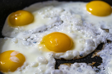 Closeup view of fried eggs which are being cooked on black frying pan in the morning at kitchen