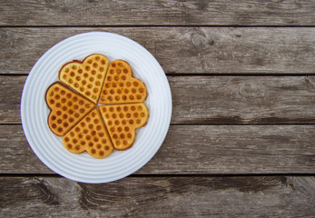 Biscuits in the form of hearts are folded into a circle on a large white plate. It's on a wooden table. View from above. There is place for inscription