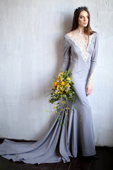 A gorgeous brunette in a gray dress embroidered with lace and stones with a long train. Bride with a bouquet in her hands. A Queen with a crown on her head. Wedding photo shoot. Rustic wedding.