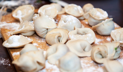 Raw homemade dumplings with minced meat on wooden board on table,  sprinkled with flour. Close up view of traditional Russian pelmeni. Selective focus
