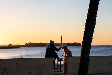 Persona al atardecer con un perro. Castillo San Sebastián al fondo, Cádiz. Atardecer © Rafael Beltrán