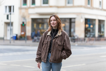 Naklejka na ściany i meble Young Caucasian Woman in Brown Jacket and Earphones Smiling at the Camera
