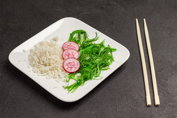 Salad with rice, radish and seaweed in white plate. Asian food. Bamboo chopsticks