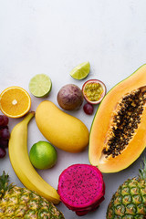 Flat lay tropical exotic fruits with copy space. Vegetarian dessert. Healthy summer food ingredients: papaya, pitaya, pineapple, orange, lime, grapes and mango.