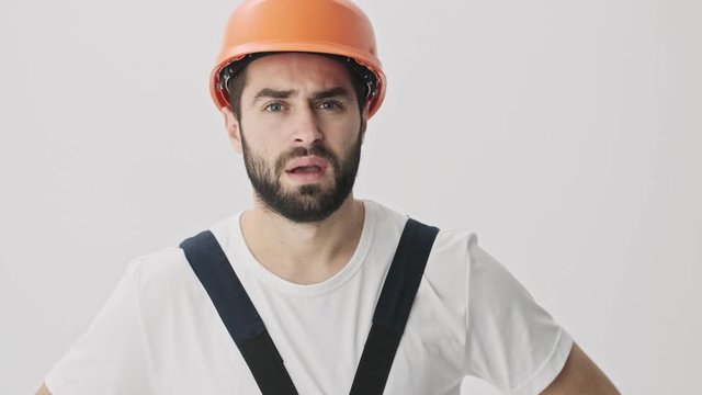 Displeased negative young bearded man builder isolated over white wall background in helmet says no