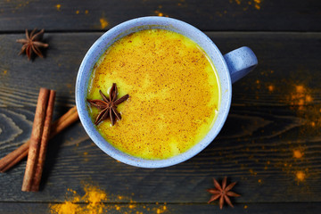 Traditional Indian drink turmeric latte or golden milk with cinnamon, star anise and turmeric on a rustic wooden table.