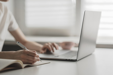 Young woman works on a laptop and takes notes in a notebook. Work in home office.