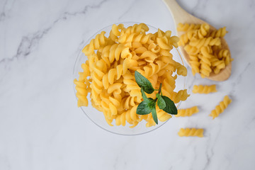 Raw uncooked italian pasta on cocktail glass over white marble. Fusilli. Diet and food concept. Top view.