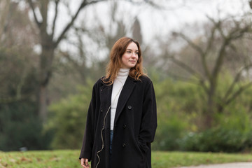 Young Woman in Long Black Wool Coat Looking Away in Public Park
