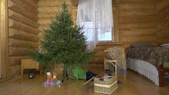 Mother with two children dresses up Christmas tree for the holiday. In the interior of the village house, a mother with children amicably take out Christmas toys and hang them on a green fluffy tree.