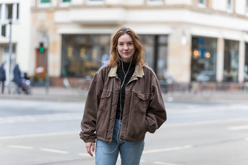 Fototapeta premium Young Woman with Earphones Looking at the Camera on City Street