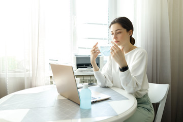 woman in medical mask, hand sanitizer on the table, working with a laptop notebook, online learning education shopping