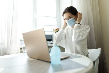 woman in medical mask, hand sanitizer on the table, working with a laptop notebook, online learning education shopping