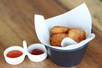 Chicken Nuggets on white paper in food box with blurred sauce on wood table.
