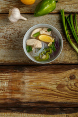 Light plate of Vietnamese Pho soup with chicken on a wooden table.