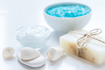 blue bath salt, body cream and shells for spa on white table background