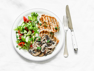 Balanced food - grilled pork with creamy mushroom sauce and fresh vegetable salad on a light background, top view
