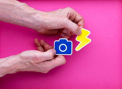 Concept dessin illustration appareil photo camera bleu et &eacute;clair flash jaune tenu par main adulte homme sur arri&egrave;re-plan rose
