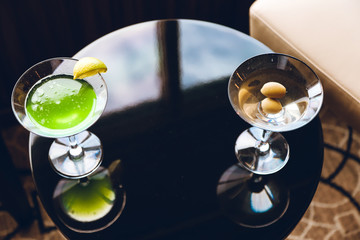 Lush green cocktail and a classic dry martini on the bar stand in a restaurant. Close up. Indoor shot.